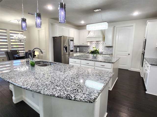 kitchen with premium range hood, a large island with sink, a sink, wall oven, and stainless steel fridge