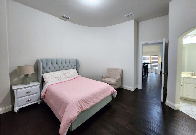 bedroom with arched walkways, visible vents, baseboards, and wood finished floors