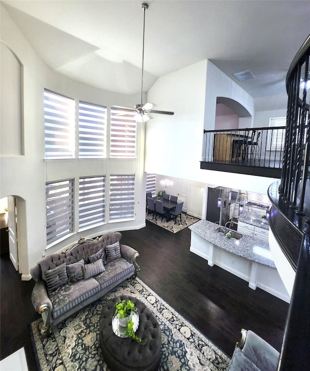 living room with wood finished floors, visible vents, arched walkways, ceiling fan, and vaulted ceiling