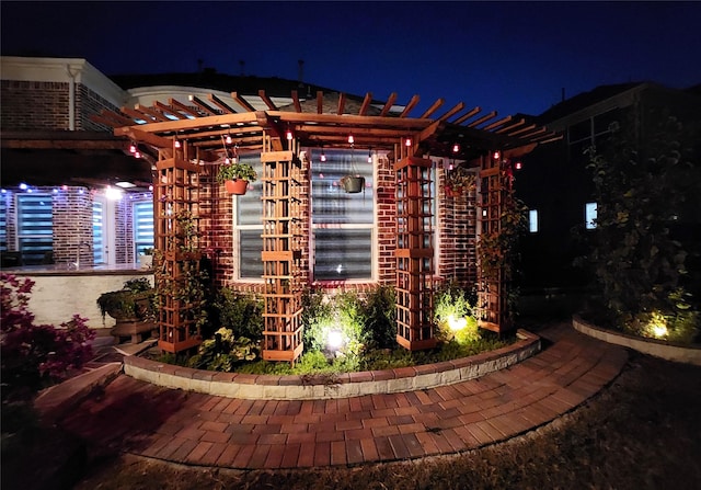 property exterior at twilight featuring brick siding and a pergola