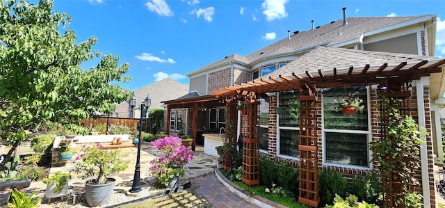 rear view of property with a pergola, fence, a shingled roof, brick siding, and a patio area