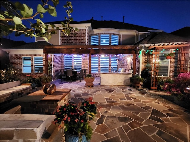 back of house at night featuring a pergola, outdoor dining area, a patio area, and brick siding