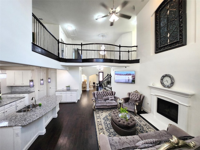 living area featuring dark wood-type flooring, a fireplace with raised hearth, a ceiling fan, a high ceiling, and stairs