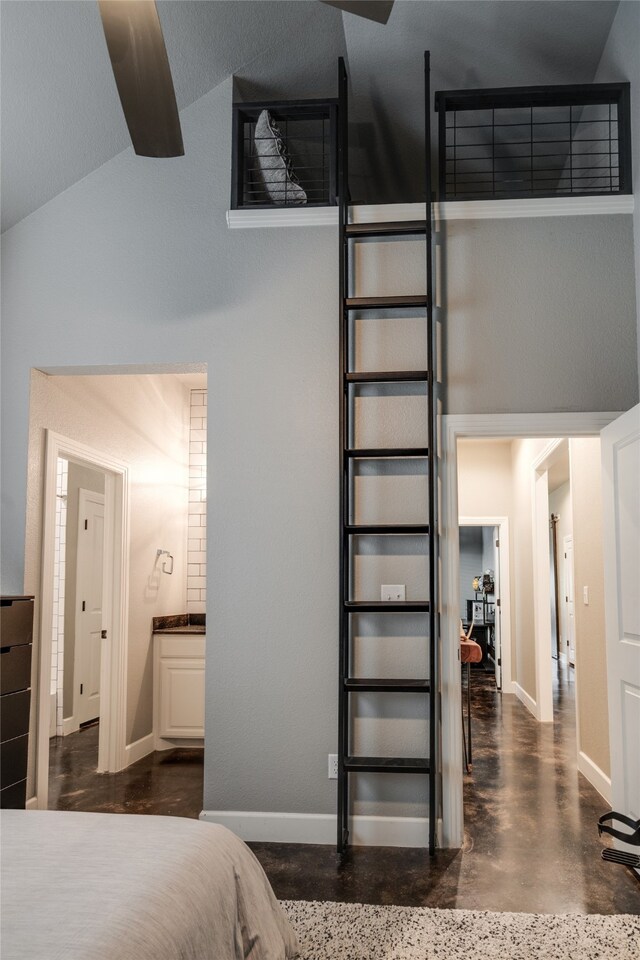 bedroom with finished concrete floors, high vaulted ceiling, ensuite bathroom, and baseboards