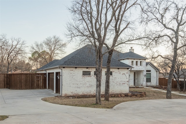 view of front of property with brick siding, a shingled roof, fence, concrete driveway, and a chimney