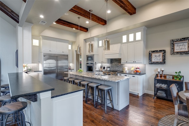 kitchen with visible vents, built in appliances, a kitchen bar, a peninsula, and custom exhaust hood