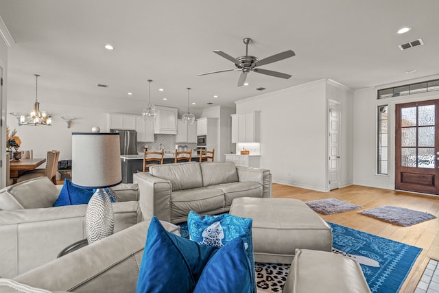 living area featuring visible vents, baseboards, light wood-type flooring, ornamental molding, and ceiling fan with notable chandelier