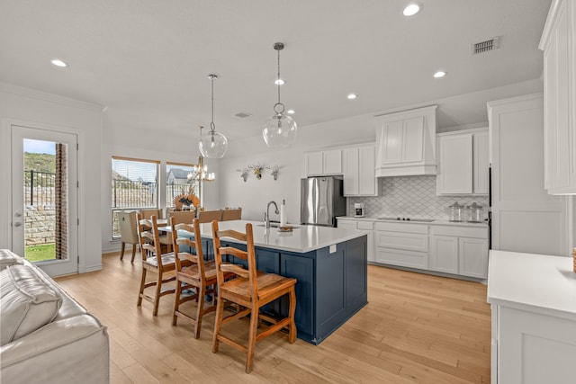 kitchen featuring decorative backsplash, white cabinets, a center island with sink, and freestanding refrigerator