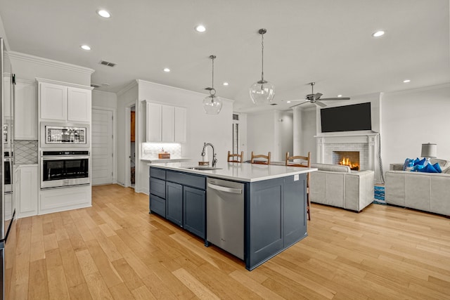 kitchen with a warm lit fireplace, a sink, stainless steel appliances, light countertops, and white cabinetry