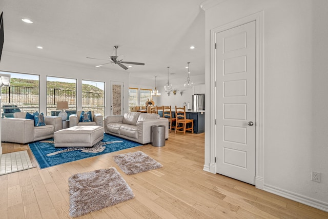 living area with baseboards, light wood-style flooring, recessed lighting, crown molding, and ceiling fan with notable chandelier