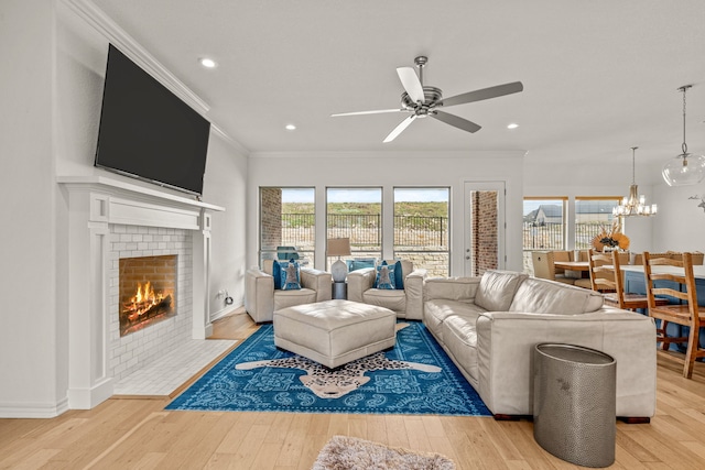 living room with ceiling fan with notable chandelier, light wood-style floors, crown molding, and a tiled fireplace