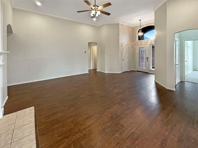 unfurnished living room featuring baseboards, ceiling fan, a fireplace, wood finished floors, and arched walkways