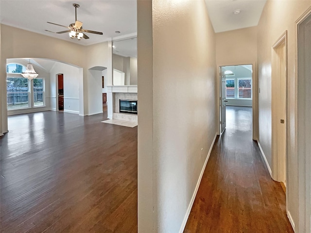 hall featuring dark wood-type flooring, arched walkways, and baseboards