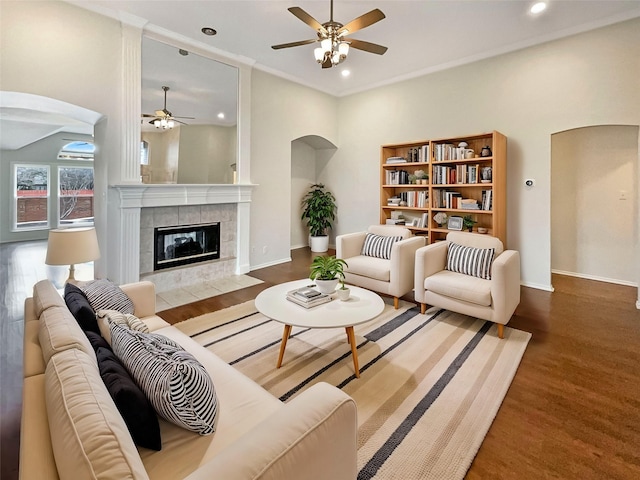 living area featuring baseboards, arched walkways, wood finished floors, and a tile fireplace