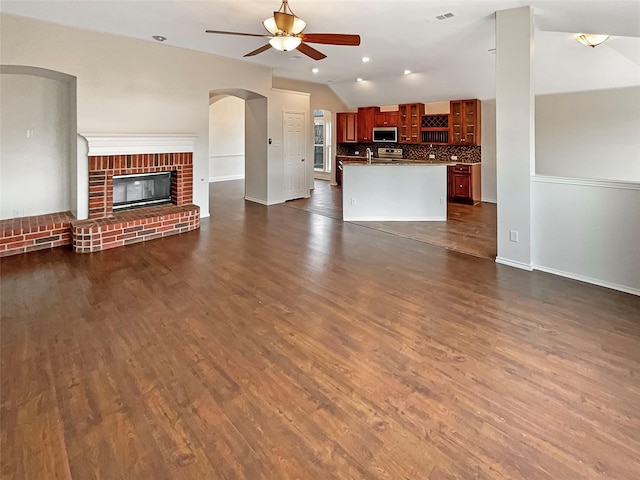 unfurnished living room with visible vents, dark wood-style floors, a fireplace, lofted ceiling, and ceiling fan