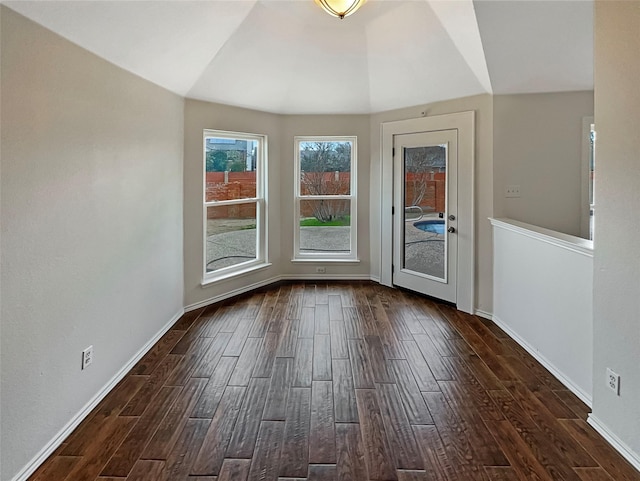 empty room featuring dark wood-type flooring, baseboards, and vaulted ceiling