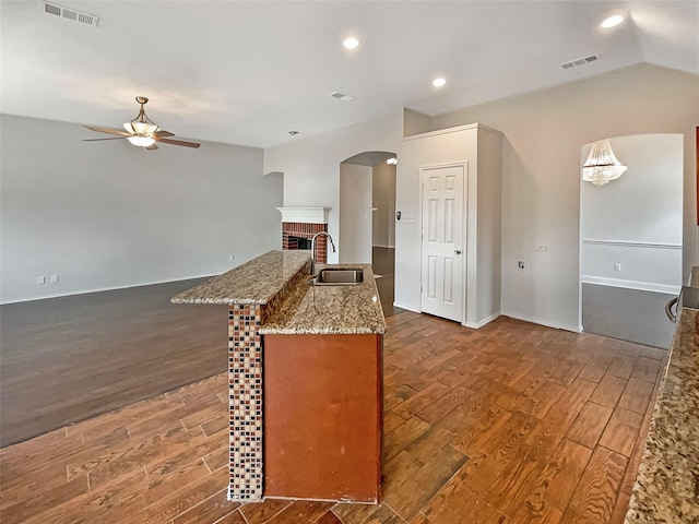 kitchen featuring a brick fireplace, visible vents, dark wood-style flooring, and a sink