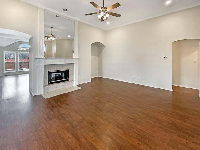 unfurnished living room with arched walkways, a tile fireplace, crown molding, and wood finished floors