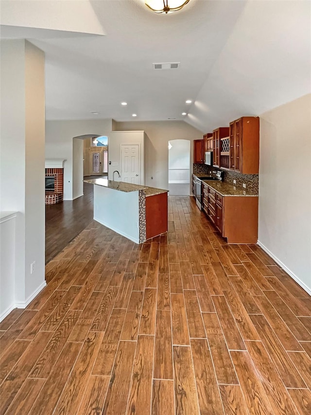 kitchen with brown cabinets, backsplash, stainless steel electric stove, dark wood-style floors, and arched walkways