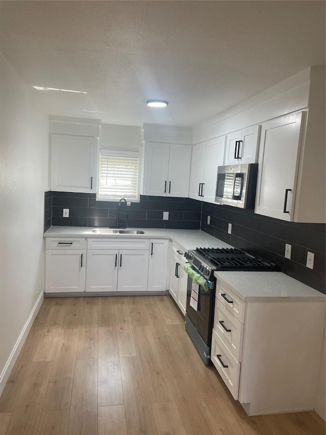 kitchen featuring light wood finished floors, a sink, appliances with stainless steel finishes, white cabinetry, and backsplash