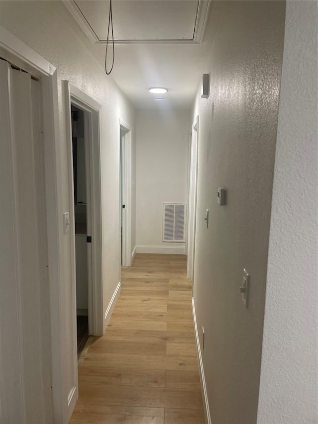 hall with visible vents, baseboards, attic access, light wood-style floors, and a textured wall