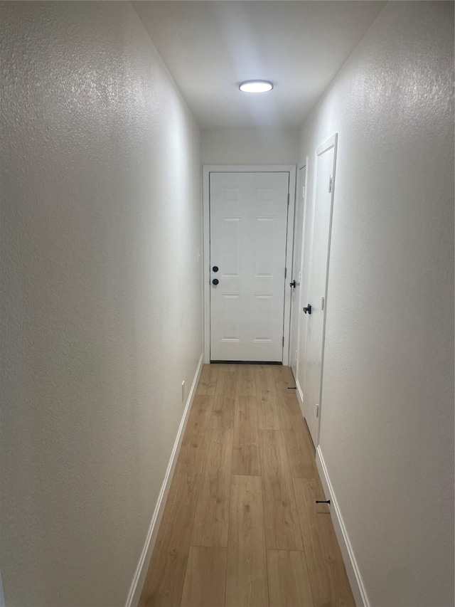 corridor with light wood-type flooring and baseboards