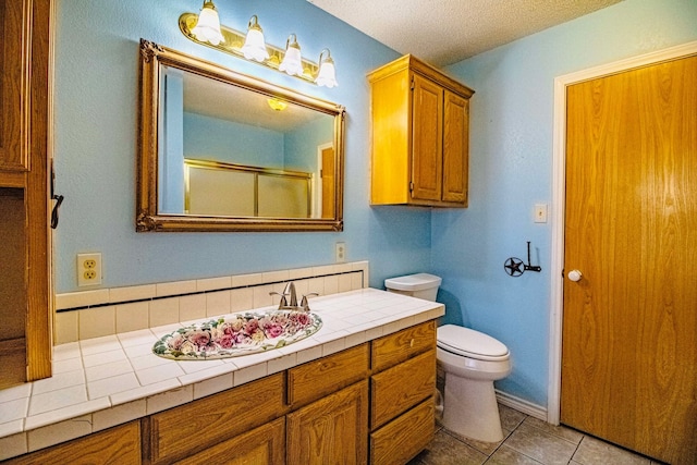 bathroom with vanity, tile patterned flooring, an enclosed shower, a textured ceiling, and toilet