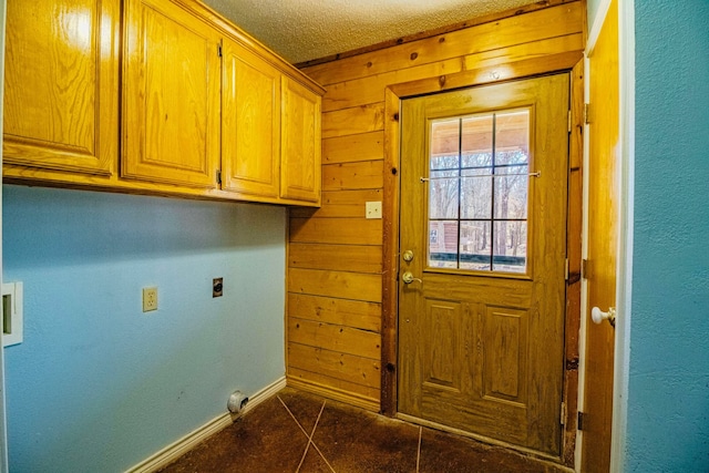 washroom featuring cabinet space, hookup for an electric dryer, a textured ceiling, and wood walls