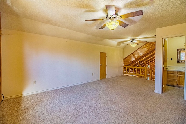 interior space with a ceiling fan, light colored carpet, baseboards, and a textured ceiling