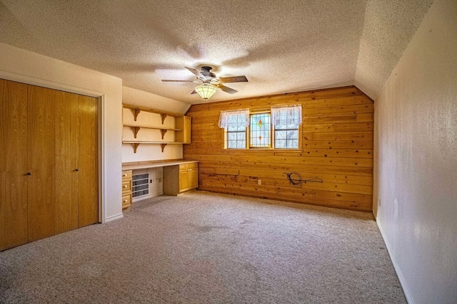 interior space with vaulted ceiling, light colored carpet, built in desk, and a textured ceiling