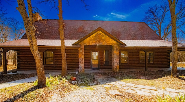 cabin featuring log siding, covered porch, and a shingled roof