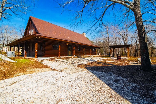 view of home's exterior featuring a porch, log siding, driveway, and a chimney