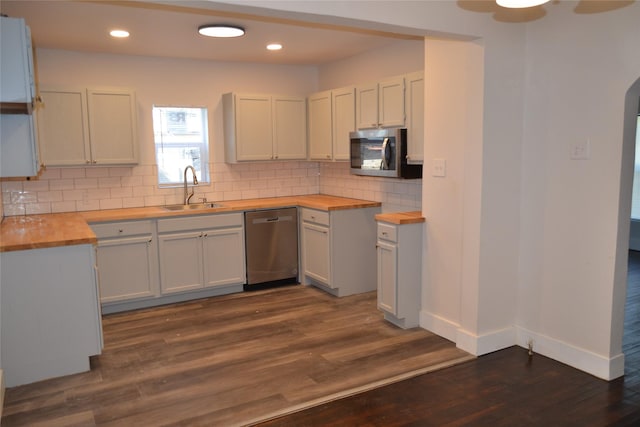 kitchen featuring arched walkways, a sink, decorative backsplash, stainless steel appliances, and butcher block counters