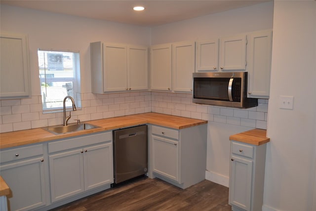 kitchen with wooden counters, a sink, stainless steel appliances, dark wood-type flooring, and backsplash