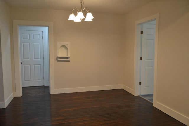 empty room with a notable chandelier, dark wood-style floors, and baseboards