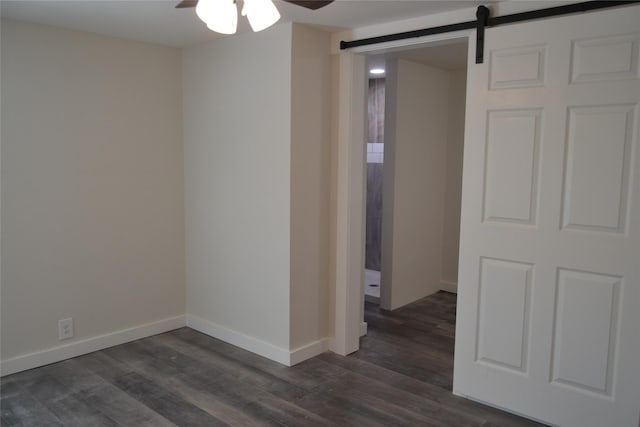 spare room with a ceiling fan, a barn door, dark wood-style floors, and baseboards