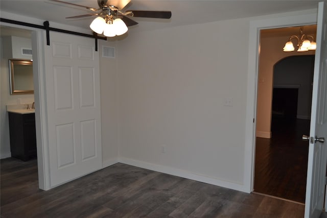 empty room with arched walkways, visible vents, dark wood finished floors, and a barn door