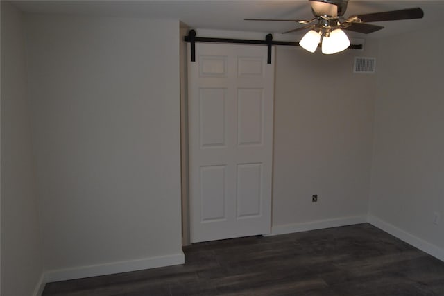 unfurnished bedroom with visible vents, baseboards, a barn door, and dark wood-style flooring