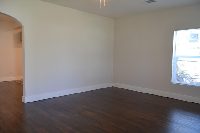 unfurnished room with arched walkways, dark wood-style floors, visible vents, and baseboards