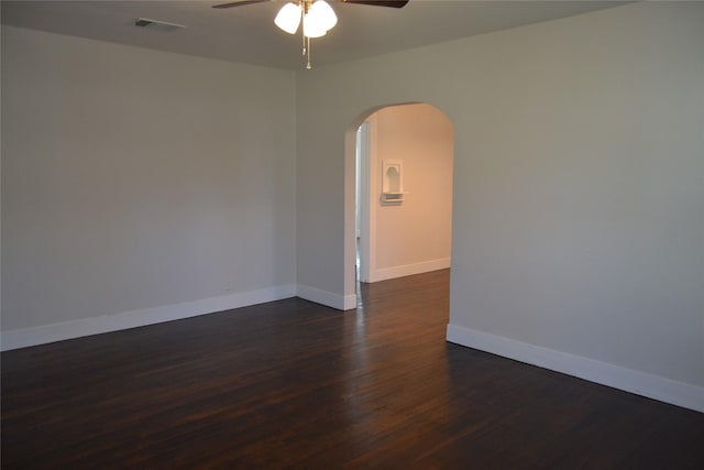 spare room with visible vents, a ceiling fan, arched walkways, baseboards, and dark wood-style flooring