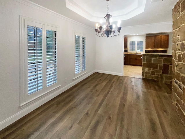 unfurnished dining area featuring dark wood finished floors, a notable chandelier, a tray ceiling, and ornamental molding