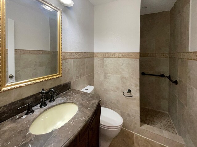 full bathroom with tiled shower, toilet, tile walls, and vanity