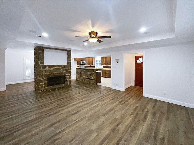 unfurnished living room featuring dark wood-style floors, baseboards, a tray ceiling, a fireplace, and ceiling fan