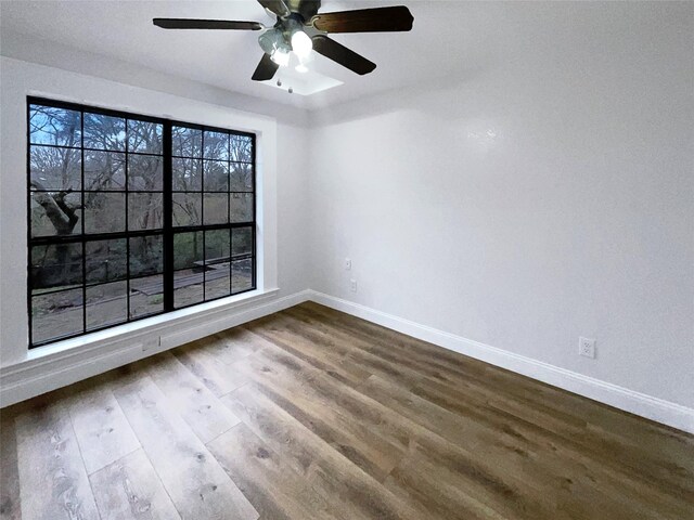 empty room featuring dark wood-type flooring, a ceiling fan, and baseboards