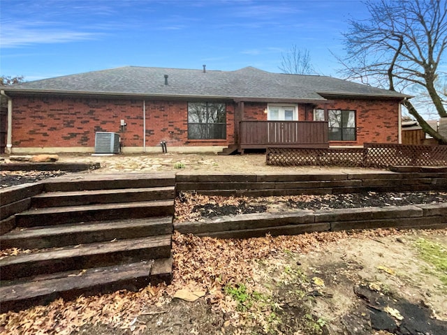 back of property with brick siding, cooling unit, a wooden deck, and roof with shingles