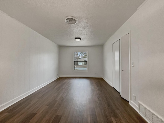 unfurnished bedroom featuring dark wood finished floors, visible vents, a textured ceiling, and baseboards