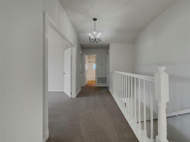 corridor featuring visible vents, a textured ceiling, carpet floors, an inviting chandelier, and baseboards