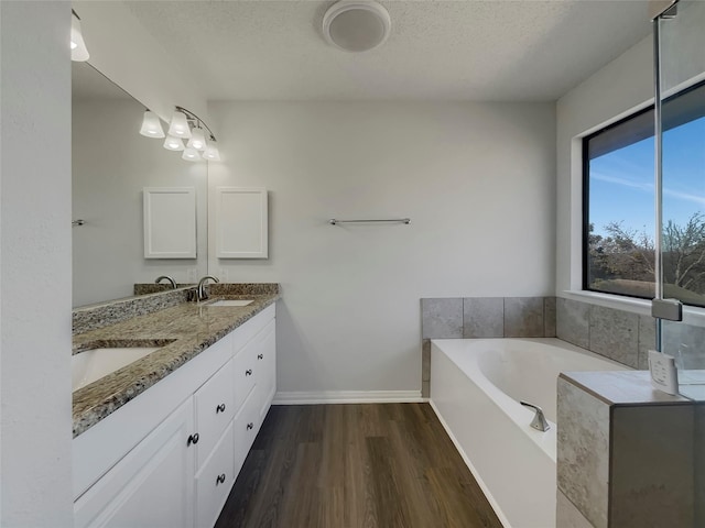 full bath featuring baseboards, a garden tub, double vanity, wood finished floors, and a textured ceiling