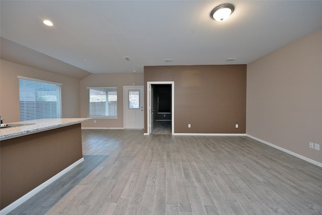 unfurnished living room with visible vents, baseboards, light wood-style flooring, and vaulted ceiling