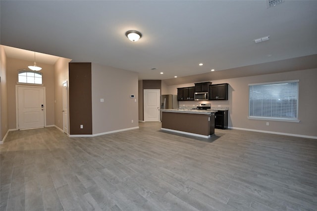 kitchen featuring open floor plan, light countertops, light wood-style flooring, appliances with stainless steel finishes, and a kitchen island with sink